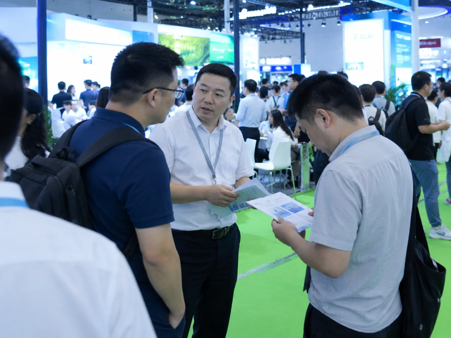 Attendees standing in an exhibition area and discussing printed material.